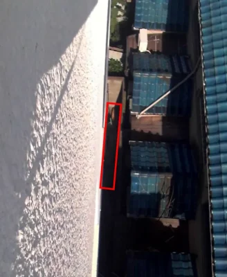 マンションの上階から敷地奥を見下ろした写真。左側に白い外壁があり、奥の赤枠内に2枚のサーフボードが置かれている。